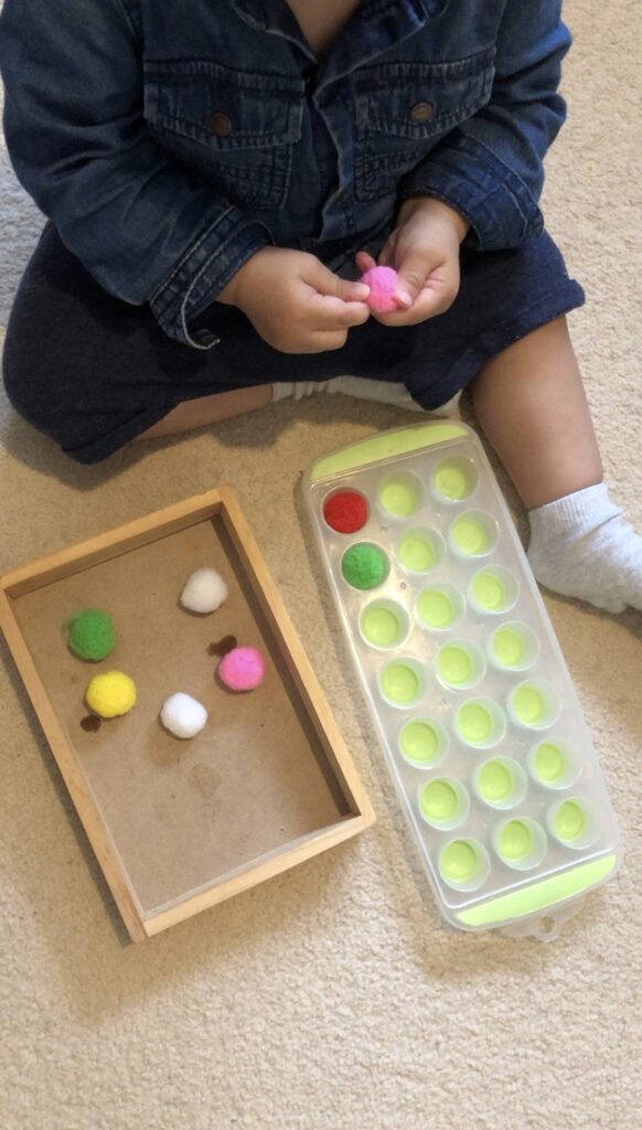 13 month old toddler concentrating on putting pompoms into holes